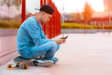 Fotobehang Young hipster guy skateboarder selfie with mobile phone while sitting on skateboard outdoors © shangarey
