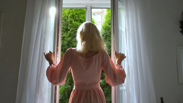 elegant woman opens window to sunny garden