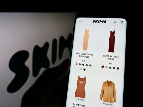 Stuttgart, Germany - 01-28-2022: Person holding cellphone with webpage of American clothing company Skims Body Inc. on screen in front of logo. Focus on center of phone display.