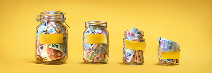 Four glass jars with yellow blank stickers, savings, cash money (euro banknotes) on yellow background - obrazy, fototapety, plakaty