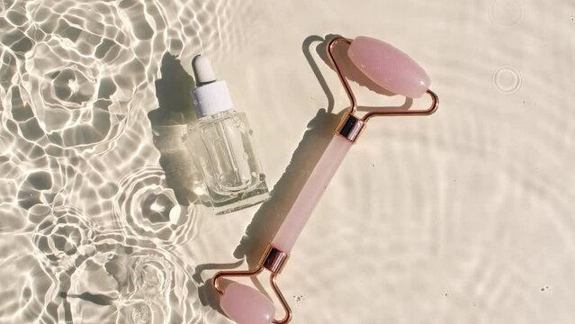Cosmetic bottle with pipette and Massage roller on water with drops. Water with reflections sunlight and shadows. Women's cosmetics skincare. Sample of layout of beauty product. 4k 