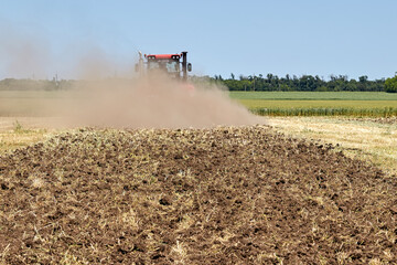 Fototapeta premium Plowed land in the field, against the backdrop of a working tractor