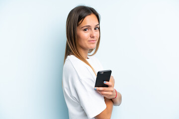 Fototapeta premium Young caucasian woman isolated on blue background holding a mobile phone and with arms crossed