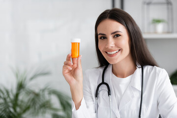 Cheerful doctor holding pills and looking at camera in clinic