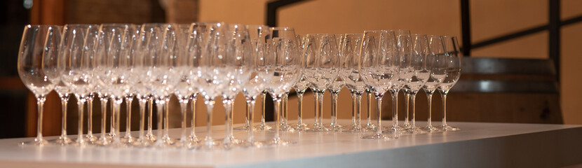 sparkling crystal wine glasses arranged in a row on a table with a white tablecloth ready for wine tasting, wine barrel in background