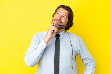Telemarketer dutch man working with a headset isolated on yellow background thinking an idea while looking up