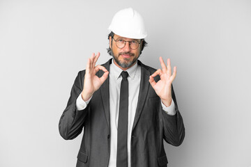 Young architect man with helmet over isolated background showing an ok sign with fingers