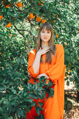 Happy pretty girl in orange dress is looking at camera by putting hand on chest  in orange garden