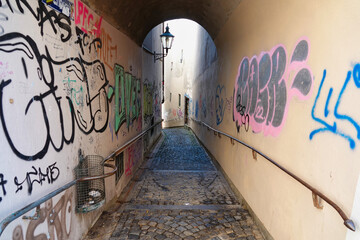 Eine alte Bogengasse mit Graffity, einem Müllbehälter und einer Laterne an der Wand