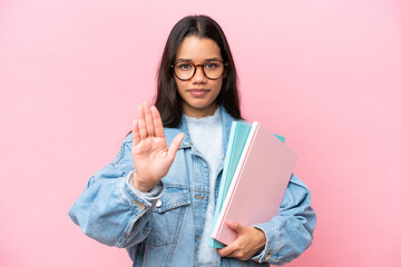 Young student Colombian woman isolated on pink background making stop gesture