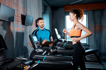young beautiful woman has workout on treadmill with personal trainer and running