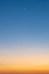 Clear blue and orange sunset sky with crescent moon.