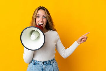 Young blonde woman isolated on yellow background shouting through a megaphone and pointing side