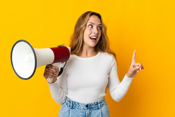 Young blonde woman isolated on yellow background holding a megaphone and intending to realizes the...