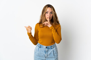 Young blonde woman isolated on blue background pointing to the side and doing silence gesture
