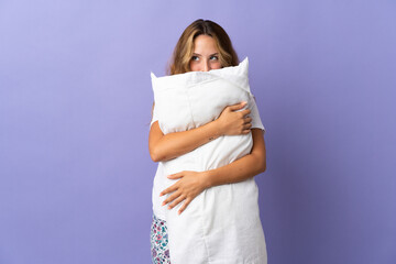 Young blonde woman isolated on purple background in pajamas and holding a pillow