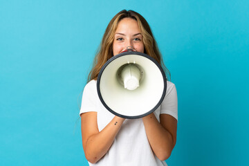 Young blonde woman isolated on blue background shouting through a megaphone