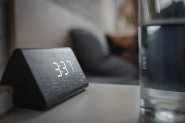 Close up view of electronic alarm clock near glass of water in bedroom