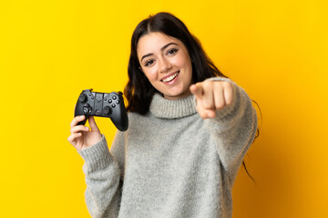 Woman playing with a video game controllerisolrted on yellow background points finger at you with a confident expression - obrazy, fototapety, plakaty