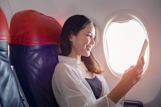 Young beautiful woman is using smartphone on airplane, travel and holidays concept