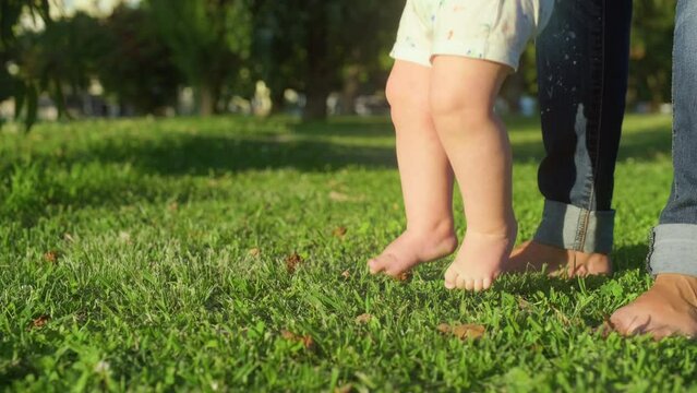 Kid is standing on the spot stomping his feet on the green grass. Bare feet of a baby on a green lawn in the park in summer.
