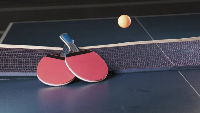 Close up shot of two rackets and bouncing ping pong ball on table tennis court with net