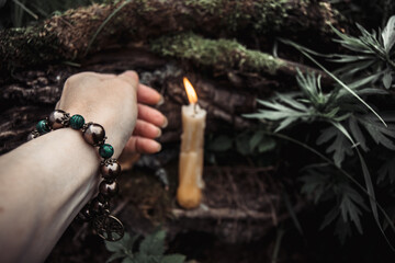 burning candles and a womans hand with a bracelet on a dark natural background. pagan wiccan, slavic traditions. Witchcraft, esoteric spiritual ritual for mabon, halloween, samhain. 