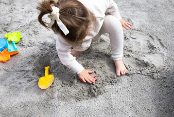 A little girl playing in the sand in the sandbox on the playground.