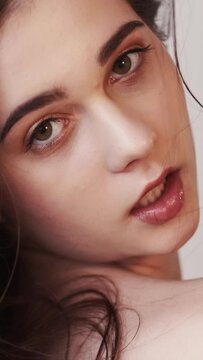 Vertical video. Natural female beauty. Fashion model shooting. Perfect skin. Smiling sensual brunette woman posing on neutral blur slow motion.