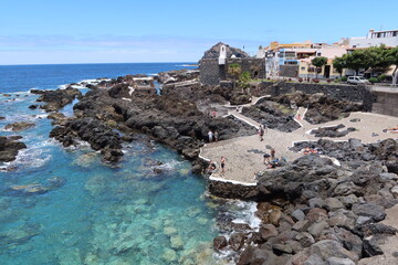 Fototapeta premium Garachico, Tenerife, Canary Islands, Spain, July 6, 2022: Tourists at the El Caleton natural pools next to the San Miguel castle in Garachico, Tenerife. Spain