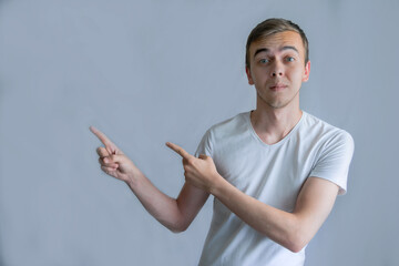 Young handsome man wearing casual white shirt pointing something on his side with his hand over gray background