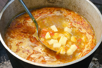 Cooking fish soup or uha in a cast iron cauldron. Delicious fish broth with vegetables. Chef stirs potatoes in the soup with a spoon. Shallow depth of field.