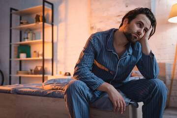 Tired man in pajama sitting on bed at night