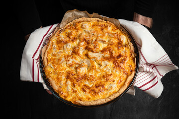 Quiche pie in chef hands on dark background. Savory tart Lorraine with cheese, chicken and mushrooms, freshly baked in oven. Traditional french cuisine. Home cooking recipe. Copy space for design