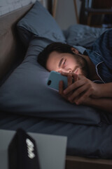 Fototapeta na wymiar Sleepless man using mobile phone near blurred alarm clock on bed at night