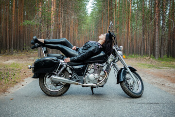 A girl in tight black leather lies on a motorcycle.