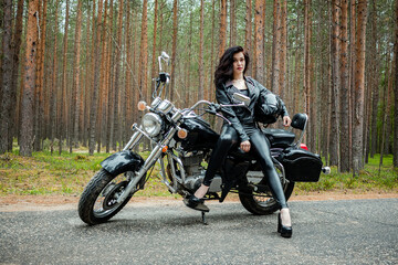 A girl in tight black leather sits on a motorcycle.