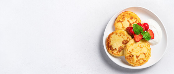 Cottage cheese pancakes with fresh strawberries, mint and cream on a gray background. Top view, copy space.