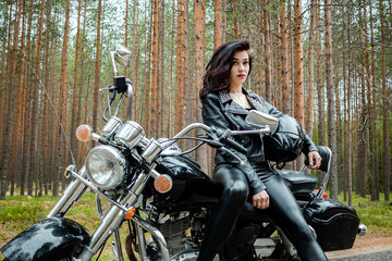 Fototapeta na wymiar A girl in tight black leather sits on a motorcycle.