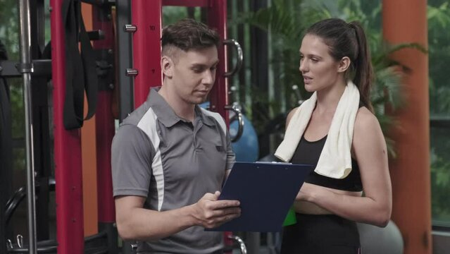 Professional male coach explaining workout plan to young sporty woman while working in gym