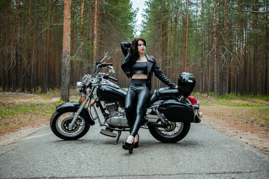 A girl in tight black leather sits on a motorcycle.