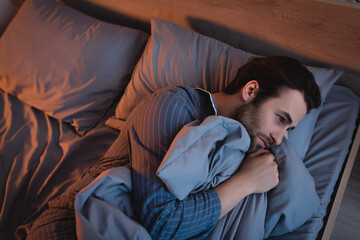 Top view of man in pajamas suffering from insomnia on bed at night
