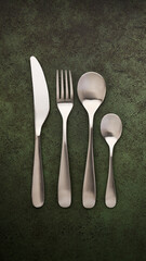 Knife, spoon, fork, teaspoon lying in a row on a dark green textured table