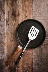Flat large pancake baking pan and kitchen steel spatula, wood background with copy space