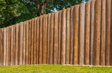 Wooden fence posts, round wood. Round timber wood fence. Wooden wall from logs a strong protection in ancient times.