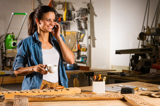 Woman Woodworker With Mobile Phone In The Workshp