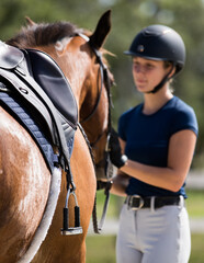 woman stands next to saddled horse. © FastHorsePhotography