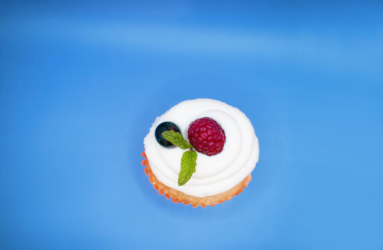Cupcake con frutos rojos como franbuesa y menta en un fondo azul aislado 