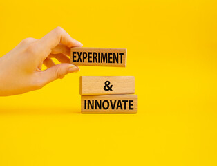 Experiment and innovate symbol. Concept words Experiment and innovate on wooden blocks. Beautiful yellow background. Businessman hand. Business and Experiment and innovate concept. Copy space.