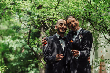 happy gay newlyweds in formal wear holding sparklers in green park.